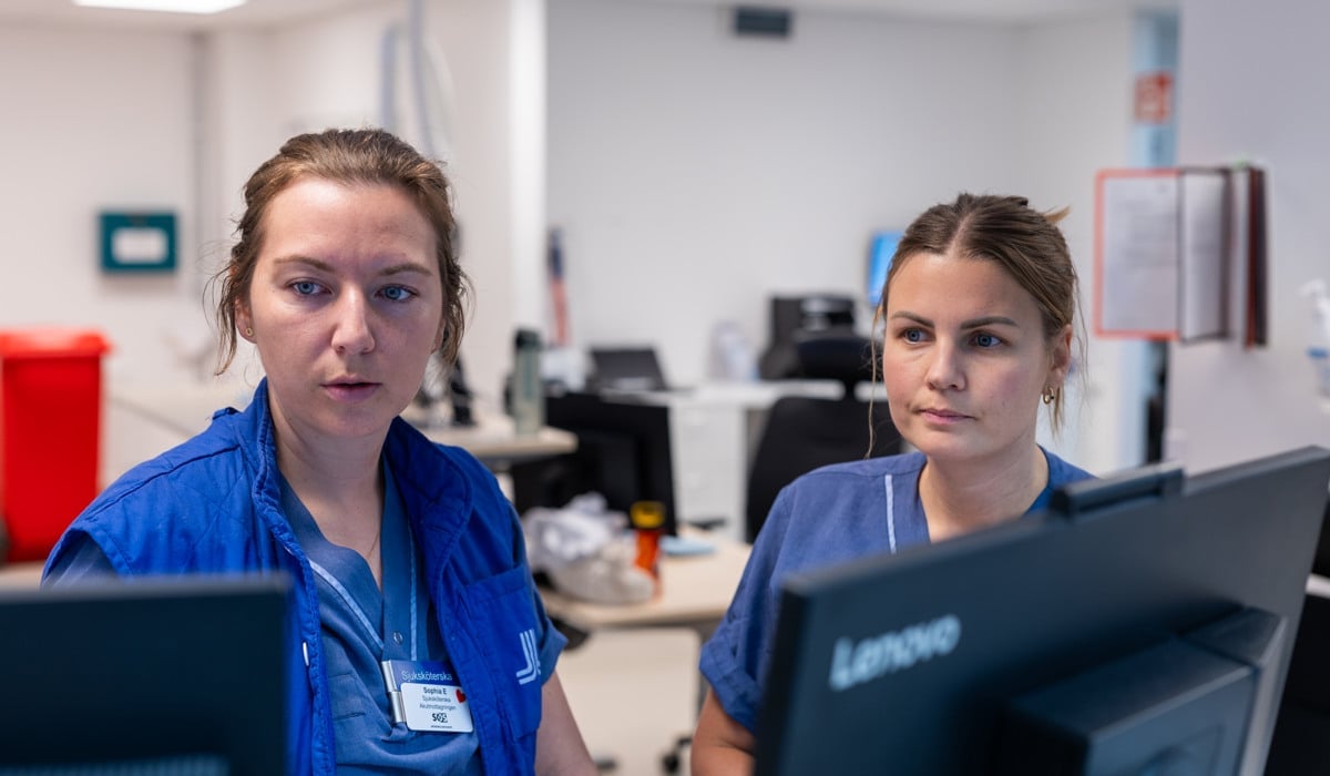 Två vårdmedarbetare står vid en arbetsstation och samtalar.