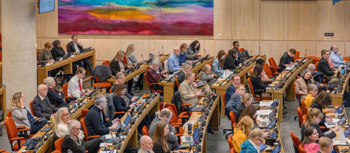 En grupp människor om utgör regionfullmäktige, som sitter vid bord i landstingssalen